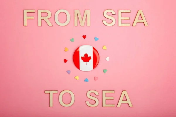 Happy Canada Day greeting card with wooden letters. Canadian motto slogan saying from sea to sea and flag with many hearts on living coral pink background. Multiculturalism concept