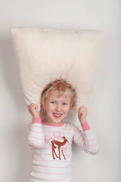 No sleeping insomnia concept. Cute funny adorable excited surprised blonde Caucasian girl child with wide open eyes playing with white soft fluffy pillow. Kid does not want to sleep