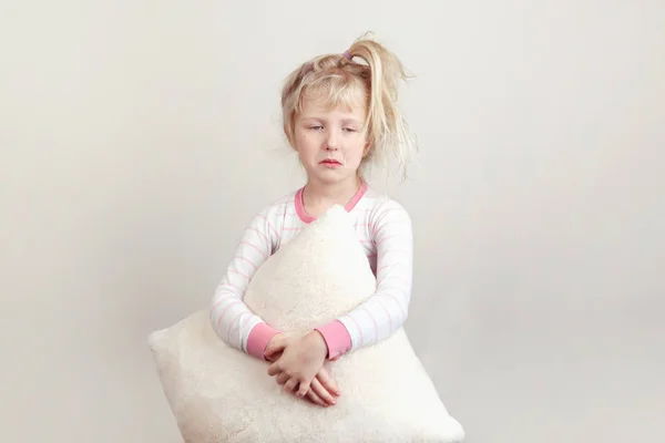 No sleeping insomnia concept. Cute funny adorable sad unhappy  blonde Caucasian girl child embraces holding white soft fluffy pillow. Kid does not want to sleep and refuses to go to bed