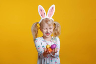 Sevimli sevimli Beyaz sarışın kız pembe Paskalya tavşan kulaklı Studio Sarı zemin üzerine yumurta holding beyaz elbiseli. Komik çocuk çocuk geleneksel Hıristiyan tatil kutluyor