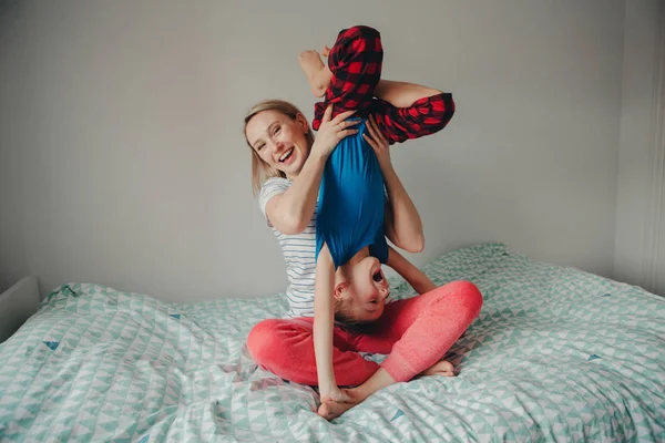 Group portrait of Caucasian mother and boy son playing together in bedroom at home. Mom holding child upside down and laughing. Family having fun. Happy childhood lifestyle.