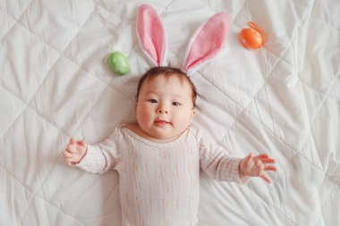 Pembe Paskalya tavşan kulakları ile renkli yumurta yatak yatak odasında yatan giyen sevimli karışık Asya bebek. Komik çocuk bebek, geleneksel Hıristiyan tatil kutluyor. Yukarıdaki üstten görüntülemek