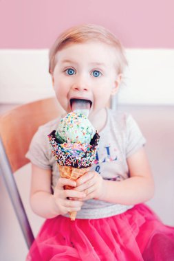 Şirin komik Beyaz sarışın bebek kız çocuğu büyük gözleme koni ile sprinkles yalama dondurma yeme ve dilini gösteren mavi gözlü. Çocukluğum mutlu bir yaşam tarzı. Lezzetli yaz gıda