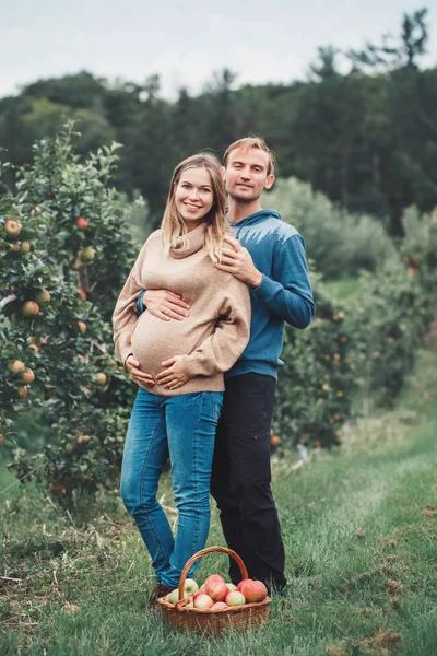 Happy healthy pregnancy and parenting. Portrait of pregnant young blonde Caucasian woman with husband on apple farm. Beautiful expecting mother and future father at countryside, rustic style