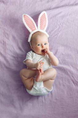 Sevimli güzel beyaz Kafkas bebek kız yatak odasında pembe mor yatakta yatan pembe Easter Bunny kulakları giyiyor. Geleneksel Hıristiyan tatili kutluyor komik çocuk bebek. Üstte görüntüle