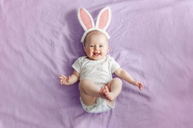 Sevimli güzel beyaz Kafkas bebek kız yatak odasında pembe mor yatakta yatan pembe Easter Bunny kulakları giyiyor. Geleneksel Hıristiyan tatili kutluyor komik çocuk bebek. Üstte görüntüle