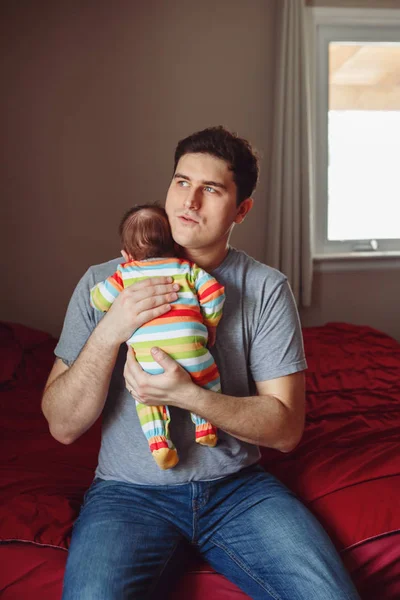 Young Caucasian father trying to calm down crying newborn baby. Male man parent holding child on his hands. Authentic lifestyle documenatry moment. Single dad family life concept.