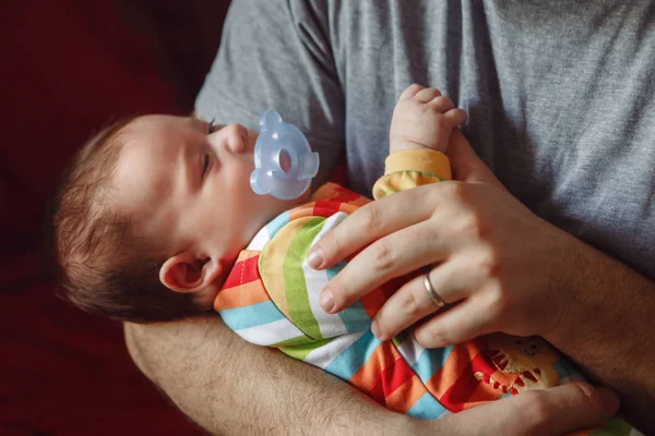 Young Caucasian father trying to calm down crying newborn baby. Male man parent holding child on his hands. Authentic lifestyle documenatry moment. Single dad family life concept.