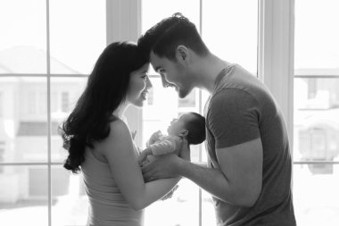 Siyah beyaz portre güzel mutlu gülümseyen Çinli Asyalı anne Kafkas baba pencere önünde karışık ırk yenidoğan bebek erkek bebek kızı tutarak. Ev yaşam tarzı otantik an