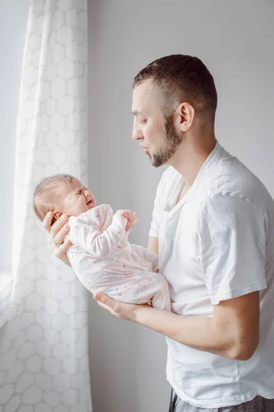 Young Caucasian father trying to calm down newborn baby. Male man parent holding rocking child on his hands. Authentic lifestyle documentary moment. Single dad family life concept.