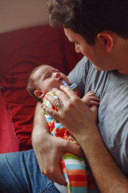 Genç beyaz bir baba yeni doğmuş bebeği sakinleştirmeye çalışıyor. Erkek ebeveyn, sallanan çocuğu elinde tutuyor. Otantik yaşam tarzı belgeselcilik anı. Bekar baba aile hayatı konsepti. 