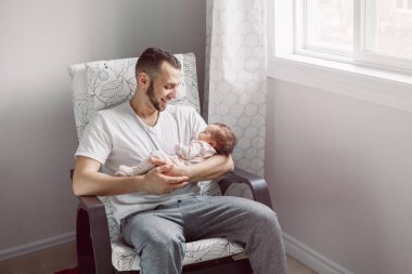 Beyaz baba yeni doğmuş bir kız bebek ile koltukta oturuyor. Ebeveyn elinde sallanan çocuk kızı oğlu tutarak. Otantik yaşam tarzı belgesel an. Bekar baba aile hayatı kavramı.
