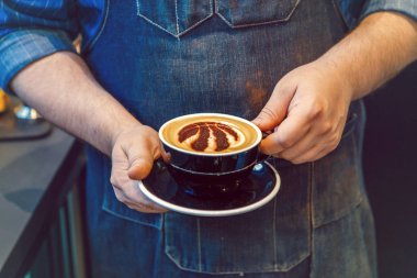 Toronto, Ontario, Kanada-Haziran 6, 2019: barista el closeup süt köpük üzerinde Toronto Raptors basketbol takımı logosu işareti ile kahve cappuccino siyah fincan tutarak.