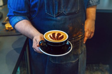 Toronto, Ontario, Kanada-Haziran 6, 2019: barista el closeup süt köpük üzerinde Toronto Raptors basketbol takımı logosu işareti ile kahve cappuccino siyah fincan tutarak.