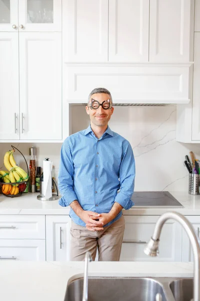 Caucasian smiling white man wearing funny kids children cat glasses standing in kitchen at home.