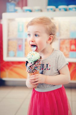 Sevimli sevimli beyaz yürümeye başlayan çocuk kız çocuk mavi gözlü dondurma büyük gözleme koni sprinkles ile holding. Bebek yalama dondurulmuş gıda. Çocukluğum mutlu bir yaşam tarzı. Lezzetli yaz tatlı