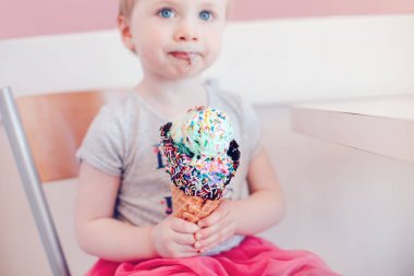 Sevimli sevimli komik Beyaz sarışın bebek kız çocuk mavi gözlü büyük gözleme koni ile renkli sprinkles yalama dondurma yemek. Çocukluğum mutlu bir yaşam tarzı. Lezzetli yaz gıda