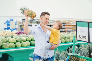 Beyaz baba baba bakkalda ananas tutarken ve küçük oğlu taşırken alışverişyaparken taze meyve alıyor. Küçük çocuk ile erkek ebeveyn snack öğle yemeği için sağlıklı bir yemek seçerek. Aile anı.