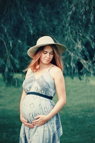 幸せな健康な妊娠 外の公園で長いドレスと無作法な国の帽子を着て妊娠中の若い白人女性の肖像画 見下ろして期待美女 — ストック写真