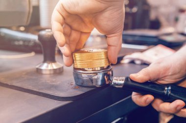 Espresso sıcak içecek yapmak için portafilter içine öğütülmüş kahve basın kahve distribütörü kullanarak barista ellerin closeup. Kafede küçük yerel işletme çalışmaları.