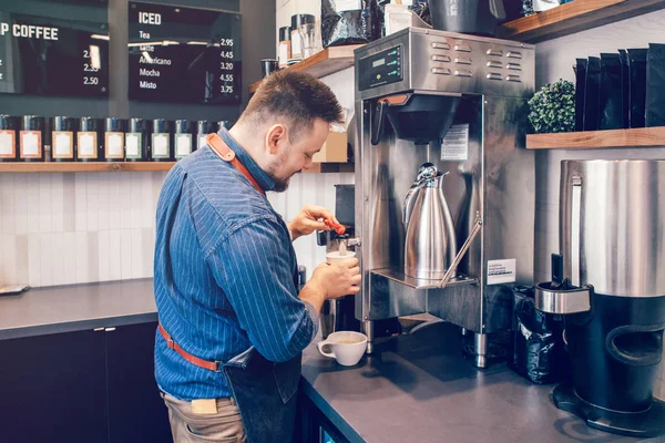 Young Caucasian barista man holding paper cup making coffee using professional machine. Server waiter pouring coffee for client customer. Small business and person at work concept