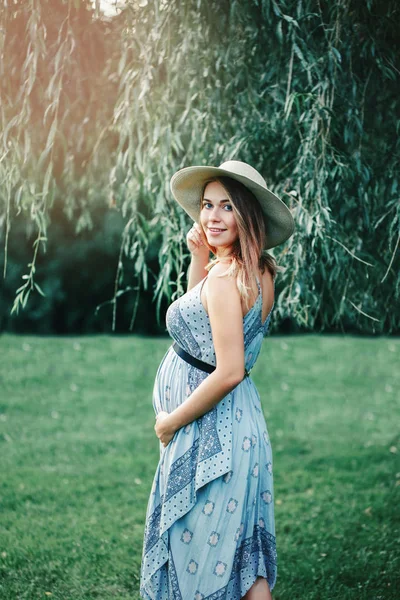 幸せな健康な妊娠 妊娠中の若い白人女性の外の公園で長い青いドレスと無作法な国の帽子を着ての肖像画 フェミニンな期待の美女 — ストック写真