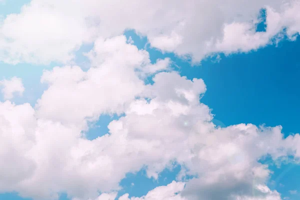 Light baby blue aquamarine sky with white pink clouds. Serene calm idyllic view of sun light coming from large big cumulus clouds. Toned with modern popular hipster style filters.