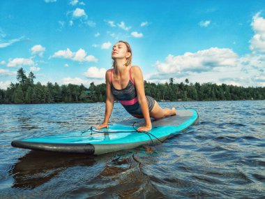Genç güzel Kafkas kadın yukarı bakan köpek yoga poz pratik yapıyor. Kız gün batımında göl su kürek sup kurulu üzerinde abs germe egzersiz yapıyor. Modern açık yaz etkinliği.