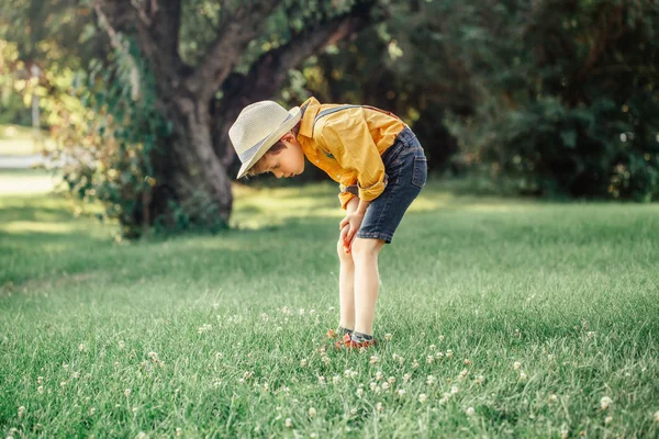 黄色いシャツとジーンズのショートパンツでかわいい愛らしい白人の少年は 公園の検索で草を見て 外で学ぶ自然を探す麦わら帽子の子供 子ども自然科学教育の概念 — ストック写真
