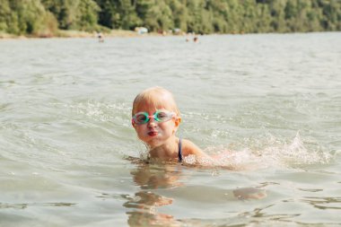 Sevimli komik Kafkas kız sualtı gözlükleri ile göl nehri yüzme. Park sahilinde suda çocuk dalışı. Otantik gerçek yaşam tarzı mutlu çocukluk. Yaz eğlencesi açık su aktivitesi.