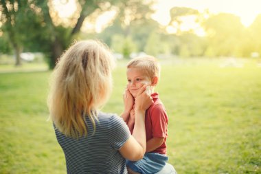 Genç Beyaz anne erkek bebek yanakları çekerek. Anne parkta yaz günü oğlu ile birlikte oturan ve sevgi ve sevgi gösteren. Mutlu aile çocukluk yaşam tarzı. Sevimli otantik an.
