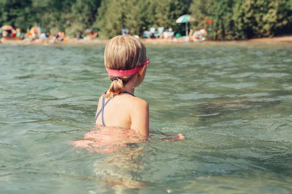 Caucasian girl swimming in lake river with underwater goggles. Child diving in water on beach. Authentic real lifestyle happy childhood. Summer fun outdoor aquatic activity. View from back.