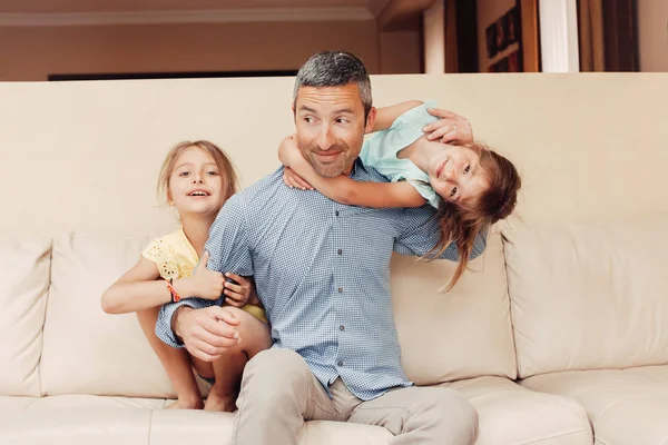 Father and daughters girls kids at home spending time together. Parent playing with children. Family having fun hugging and laughing. Real people lifestyle.  Fathers day holiday concept.