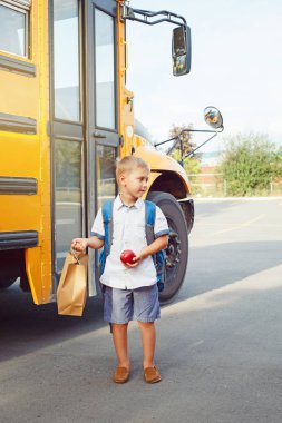 1 Eylül günü sarı otobüs yakınında sırt çantası ve elma ile Komik sevimli mutlu Kafkas çocuk öğrenci çocuk. Eğitim ve okul kavramına geri dönelim. Çocuk öğrenci öğrenmeye ve çalışmaya hazır. 