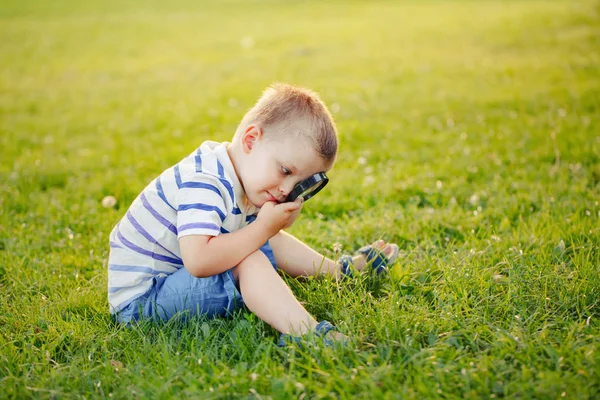 Милый Очаровательный Кавказский Мальчик Смотрит Траву Парке Через Увеличительное Стекло — стоковое фото