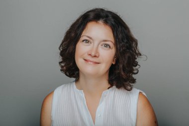 Kıvırcık koyu saçlı güzel gülümseyen esmer Kafkas orta yaşlı kadının Stüdyo baş çekim portre. Beyaz gömlek casual tarzı modeli gerçek kişi. 