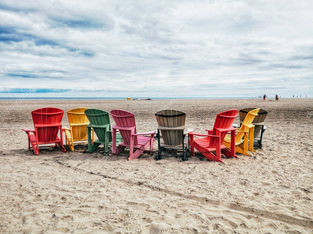 Eight many colorful red, brown and yellow wooden muskoka Adirondack chairs in row on beach outside. Concept of relaxation and calm talk conversation among friends or family.
