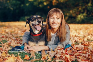 Sonbaharda sarı yaprakların arasında uzanan ve evcil köpeğine sarılan güzel, mutlu beyaz kadın portresi. En iyi arkadaşlar dışarıda eğleniyor. Evcil hayvanlarla dostluk.