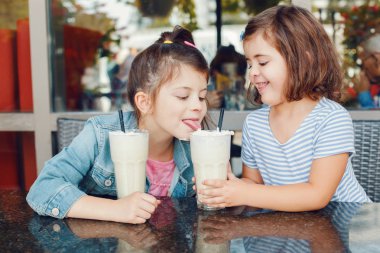 İki komik Kafkasyalı anaokulu kız kardeşi kafede milkshake içerler. Arkadaşlar birlikte eğleniyor. Çocuklar için soğuk yaz tatlısı. Mutlu otantik çocukluk yaşam tarzı. 