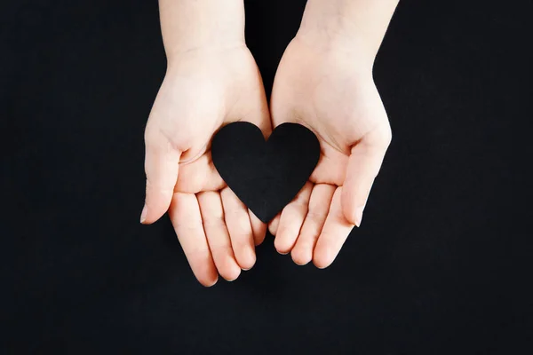 White human hands holding black paper heart on dark background. Person support activist of USA movement black lives matter. People protest against racism. Blackout Tuesday 2020.