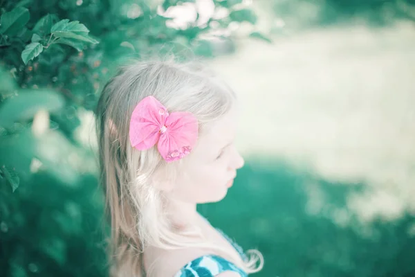 Portrait of little blonde Caucasian girl with pink hair bow. Pretty pensive sad child kid. Girly girl with red hair clip looking away. Lonely child. Soft selective focus. Blurry background.