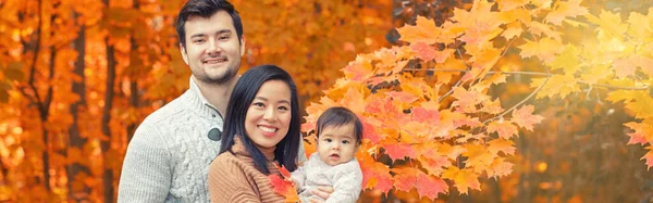 Asian Chinese mother and Caucasian father dad with baby girl in autumn fall park. Family together outdoor in nature. Seasonal holiday and authentic lifestyle. Banner header for website.