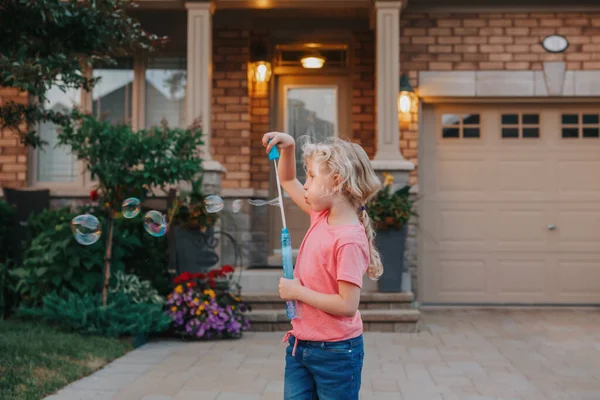 若い白人の少女が家の庭でシャボン玉を吹いていた 日没の屋外で楽しい時間を過ごしている子供 本物の幸せな子供時代の魔法の瞬間 子供のためのライフスタイル季節活動 — ストック写真