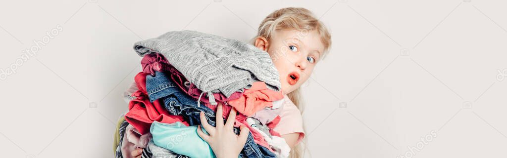 Mommy little helper. Funny cute girl child arranging organazing clothing. Kid holding messy stack pile of clothes things. Home chores housework. Web banner header for website.