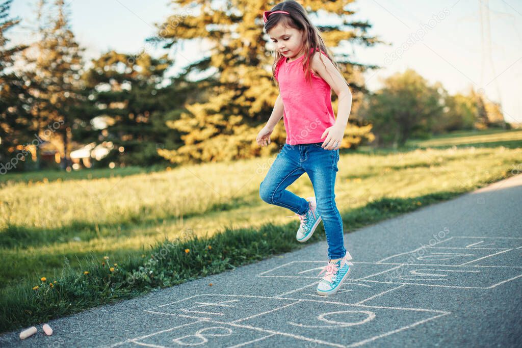 Cute adorable little young child girl playing hopscotch outdoor. Funny activity game for kids on playground outside. Summer backyard street sport for children. Happy childhood lifestyle.