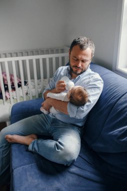 Orta yaşlı beyaz bir baba yeni doğmuş bebeği şişe sütle besliyor. Sallanan çocuğu elinde tutan bir ebeveyn. Otantik yaşam tarzı gerçek bir an. Bekar baba aile hayatı konsepti..