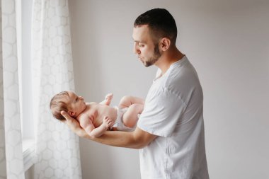 Yeni doğmuş bebeği tutan mutlu beyaz bir baba. Erkek sakallı adam, ebeveyn, sallanan küçük kız oğlu ellerinde. Otantik yaşam tarzı samimi anı. Genç baba aile hayatı konsepti.