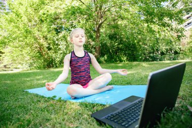 İnternette yoga yapan bir kız çocuğu. İnternetteki video spor antrenmanı. Çocuk dizüstü bilgisayarla spor yapmayı öğreniyor. Yeni normal. Coronavirus 'ta sosyal uzaklık ve eğitim. Stres atma kavramı.
