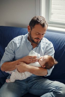 Orta yaşlı beyaz bir baba yeni doğmuş bebeği sütle besliyor. Sallanan çocuğu elinde tutan bir ebeveyn. Otantik yaşam tarzı gerçek bir an. Babalar Günü tatili.