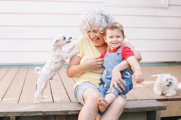 Grandmother sitting with grandson boy on porch at home backyard. Bonding of relatives and generation communication. Old woman with baby having fun spending time together outdoor.